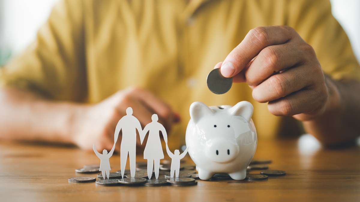 businessman putting coin on the piggybank and paper family on table