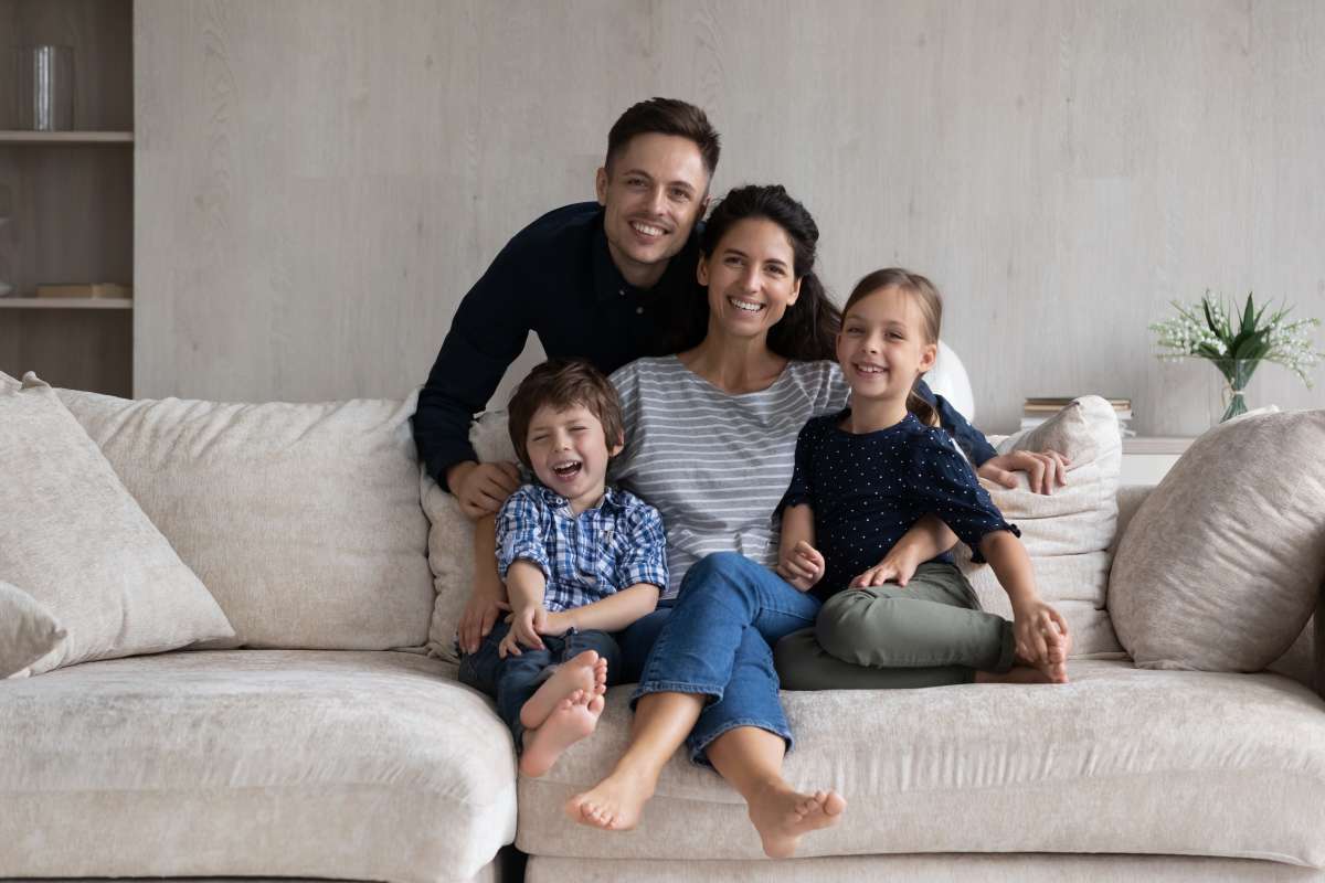 Beautiful couple with little children pose for photo. Preschool kids sit on sofa with Hispanic parents at home smile look at camera. 